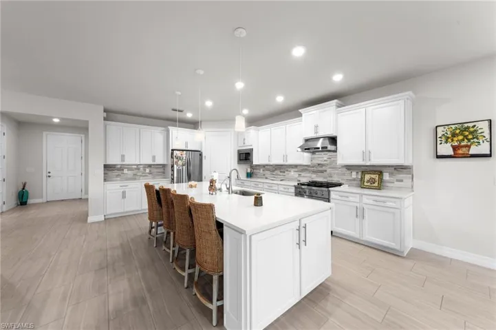 Kitchen featuring a breakfast bar area, hanging light fixtures, white cabinetry, a kitchen island with sink, and stainless steel appliances