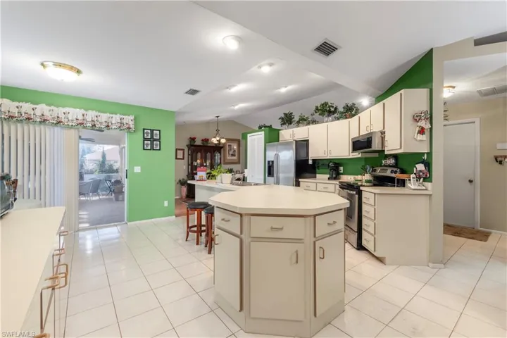 Kitchen with a sink, dishwasher, an island with sink, light countertops, and vaulted ceiling