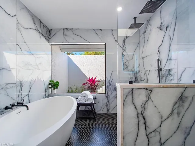 Bathroom with a marble like finish shower, a freestanding tub, and stone wall