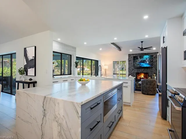 Kitchen with two tone cabinetry, a large wood burning fireplace, light stone counters, open floor plan, and upgraded appliances