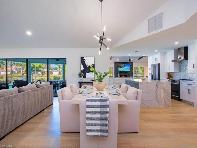 Living room featuring light wood-plank tile finished floors, vaulted ceiling, suspended lighting, and ceiling fan