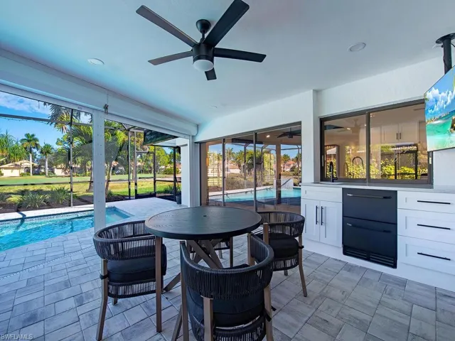 Outside pavered lanai with custom bar and fridge drawers, ceiling fan, and a heated swimming pool