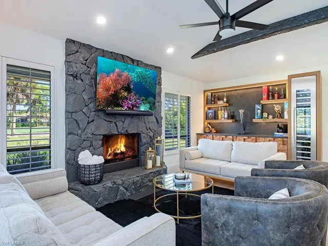 Living room with a wood burning fireplace, custom built in bar, vaulted ceiling, recessed lighting, ceiling fan, and wood-plank tile finished floors