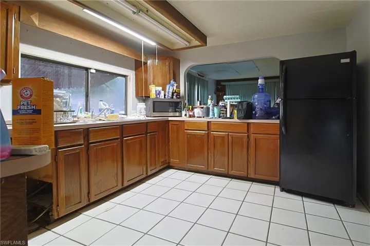Kitchen with freestanding refrigerator, light countertops, stainless steel microwave, wood finish cabinetry, and light tile patterned floors