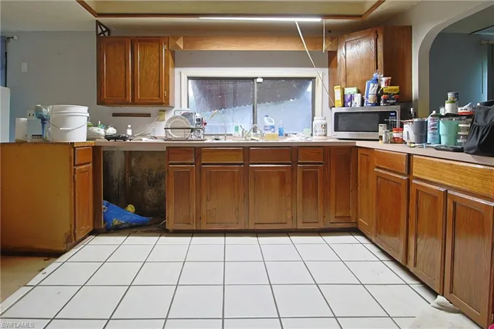 Kitchen featuring wood finish cabinets, light countertops, stainless steel microwave, arched walkways, and light tile patterned floors