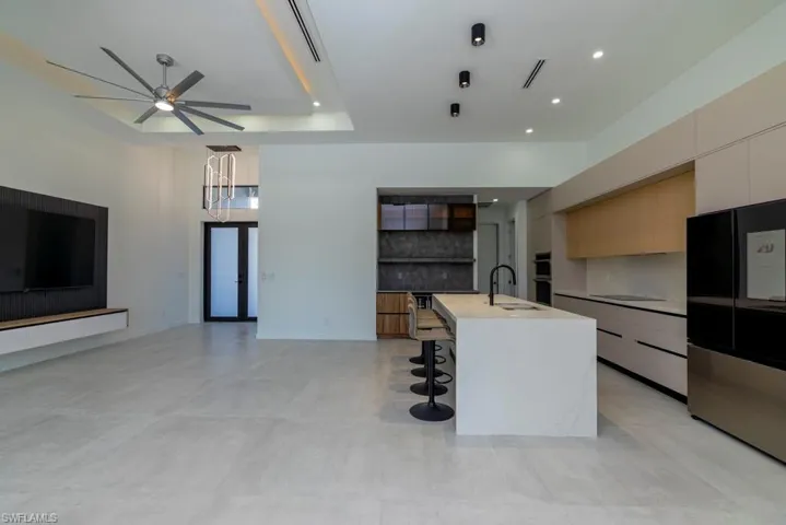 Kitchen featuring glass insert cabinets, concrete floors, a center island with sink, light stone countertops, and recessed lighting