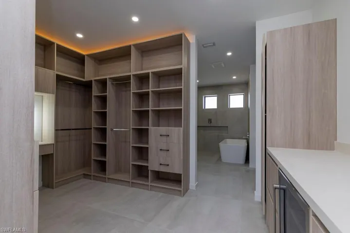 Kitchen with a center island with sink, modern cabinets, light stone countertops, wine cooler, and recessed lighting