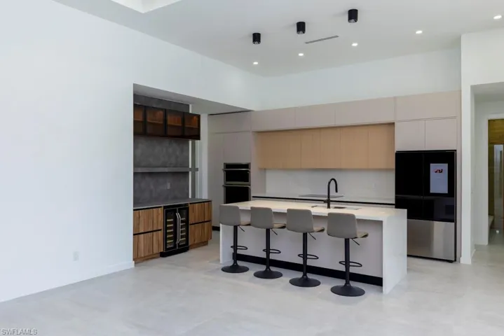 Unfurnished living room with a raised ceiling, finished concrete flooring, recessed lighting, wine cooler, and bar with sink