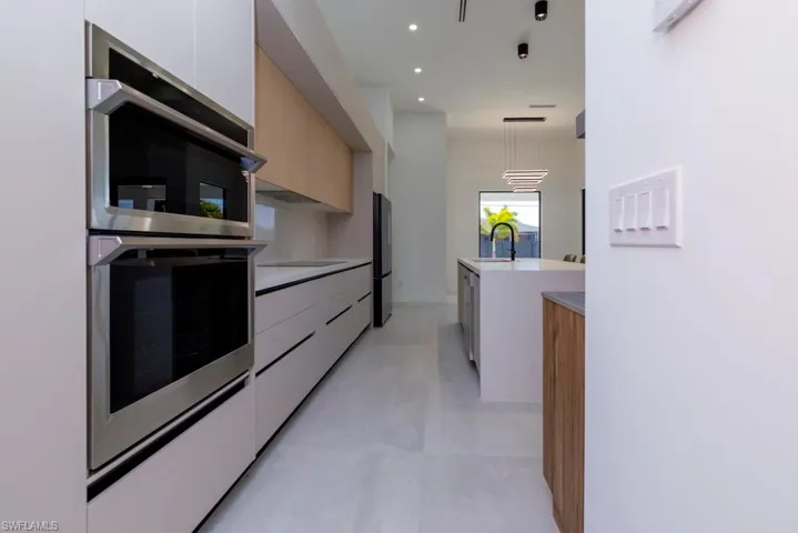 Kitchen featuring modern cabinets, freestanding refrigerator, light stone counters, decorative light fixtures, and stainless steel dishwasher
