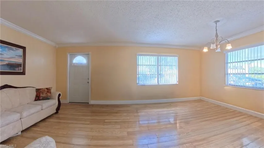 Living room featuring healthy amount of natural light, ornamental molding, a textured ceiling, a chandelier, and light wood-type flooring