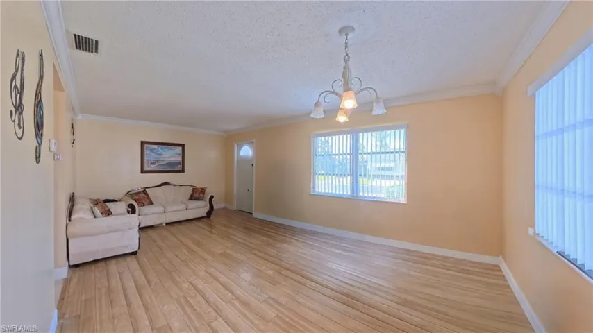 Living area with crown molding, a textured ceiling, a chandelier, and light wood finished floors