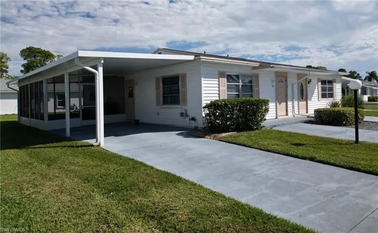 View of front facade with a front yard, a carport, concrete driveway, and a sunroom