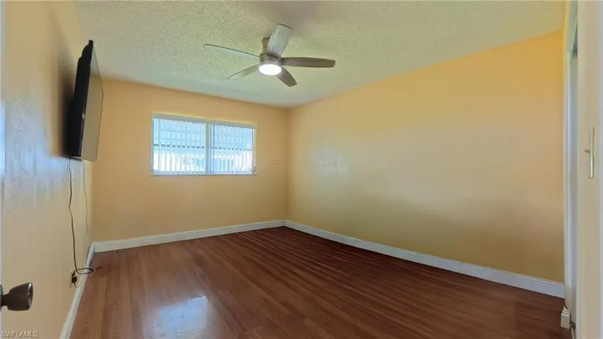 Empty room featuring a textured ceiling, dark wood-style flooring, and a ceiling fan