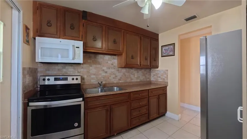 Kitchen with appliances with stainless steel finishes, decorative backsplash, light tile patterned floors, and brown cabinetry