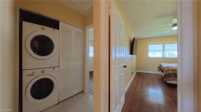 Laundry room featuring estacked washer and dryer, a textured ceiling, a ceiling fan, and wood finished floors