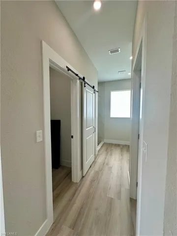 Unfurnished room with a barn door, light wood-style floors, a tray ceiling, recessed lighting, and a ceiling fan