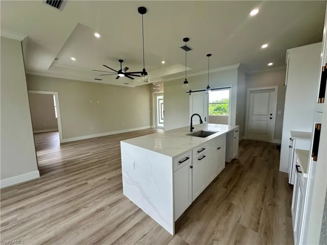 Kitchen with a tray ceiling, crown molding, recessed lighting, light wood-style flooring, and white cabinetry