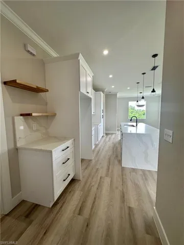 Kitchen with light wood-style flooring, light stone countertops, white cabinetry, decorative light fixtures, and open shelves