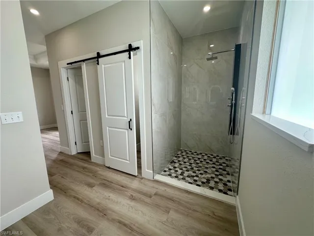 Corridor with a textured wall, a barn door, light wood finished floors, and recessed lighting