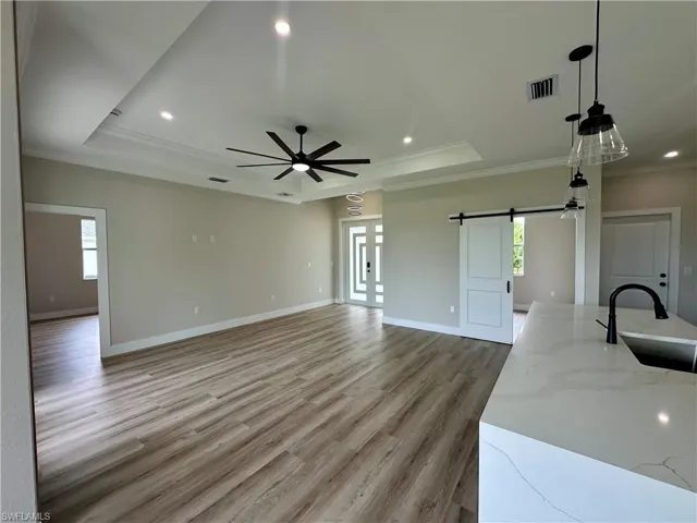 Unfurnished living room with a barn door, crown molding, light wood finished floors, a raised ceiling, and recessed lighting