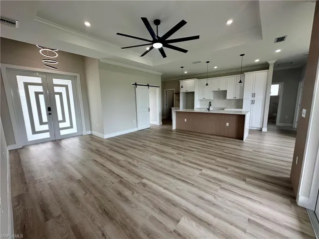 Unfurnished living room featuring a barn door, a raised ceiling, ceiling fan, crown molding, and light wood-style flooring