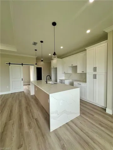 Kitchen with a barn door, crown molding, white cabinets, a large island, and recessed lighting