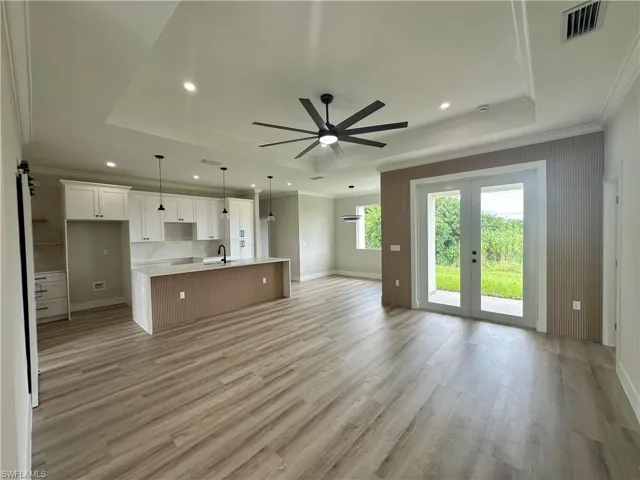 Unfurnished living room featuring a tray ceiling, ornamental molding, light wood-type flooring, a ceiling fan, and recessed lighting