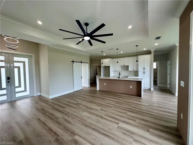 Unfurnished living room with a barn door, a tray ceiling, ornamental molding, recessed lighting, and light wood-type flooring