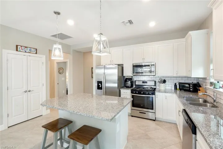 Kitchen with stainless steel appliances, a kitchen breakfast bar, a center island, white cabinets, and light stone counters