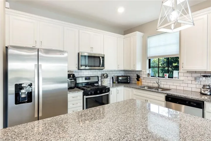 Kitchen featuring stainless steel appliances, white cabinetry, light stone countertops, backsplash, and hanging light fixtures