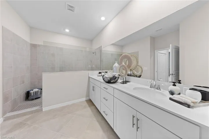 Full bathroom featuring a walk in shower, double vanity, and light tile patterned floors