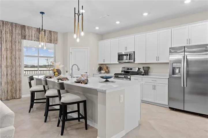 Kitchen with stainless steel appliances, white cabinets, a kitchen breakfast bar, pendant lighting, and a kitchen island with sink