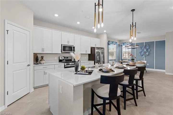 Kitchen featuring white cabinets, stainless steel appliances, a breakfast bar, an island with sink, and decorative light fixtures