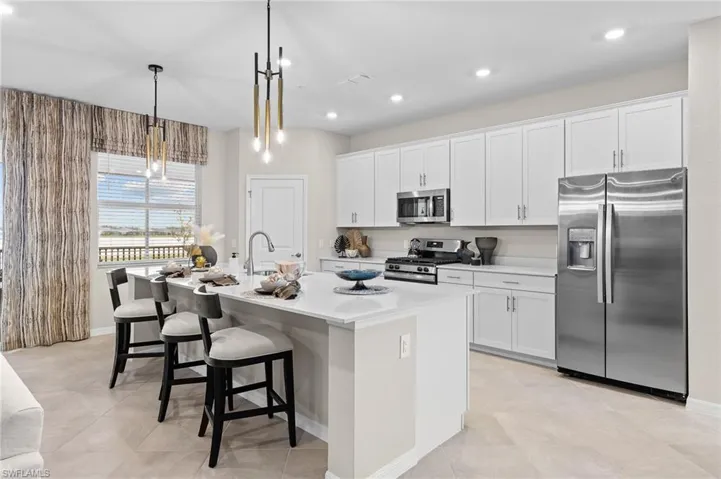 Kitchen featuring appliances with stainless steel finishes, white cabinetry, a breakfast bar, an island with sink, and pendant lighting