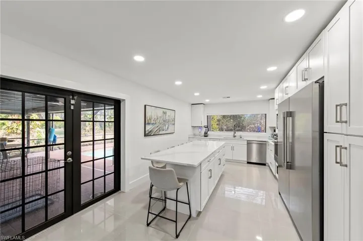 Kitchen with stainless steel appliances, a kitchen island, white cabinets, recessed lighting, and a breakfast bar area