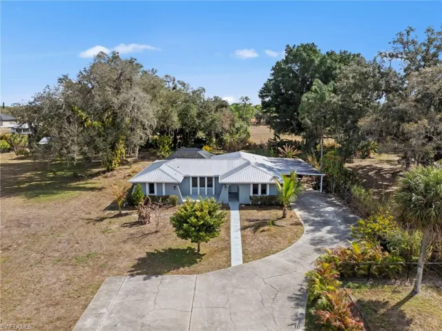 Single story home featuring concrete driveway, a metal roof, an attached carport, and view of wooded area