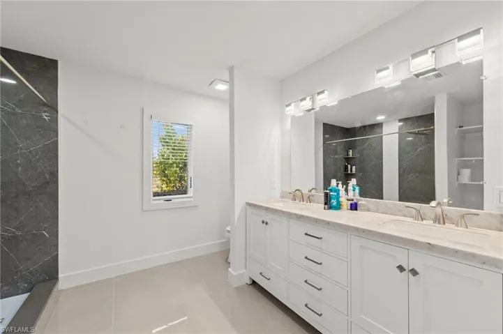 Bathroom featuring a marble finish shower, double vanity, and light tile patterned floors