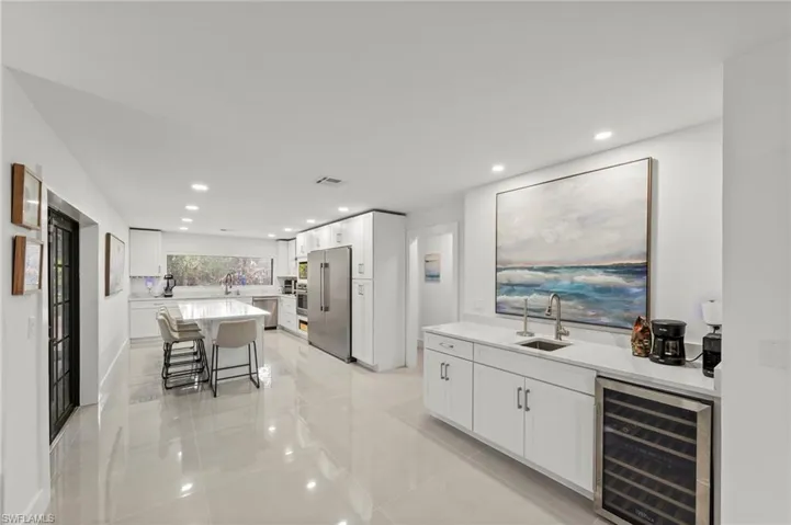 Indoor wet bar with white cabinets, wine cooler, light stone counters, stainless steel appliances, and recessed lighting
