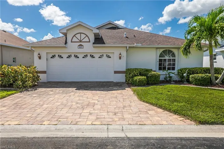 Stucco exterior featuring a dual-car garage with arched decorative detailing, paver driveway, and an arched transom window