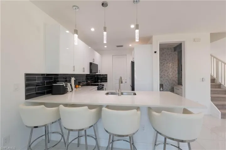 Kitchen with a peninsula, white cabinets, hanging light fixtures, black appliances, and a kitchen breakfast bar