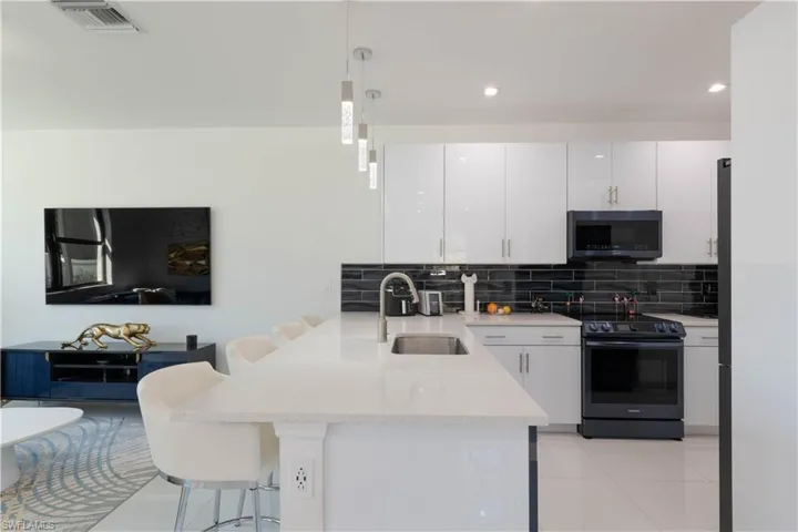 Kitchen with a peninsula, a kitchen breakfast bar, white cabinetry, black / electric stove, and decorative light fixtures