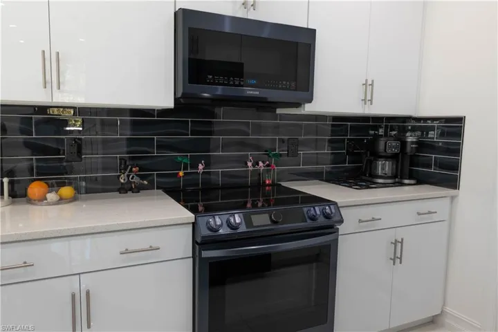 Kitchen featuring black range with electric cooktop, white cabinetry, light stone counters, and decorative backsplash