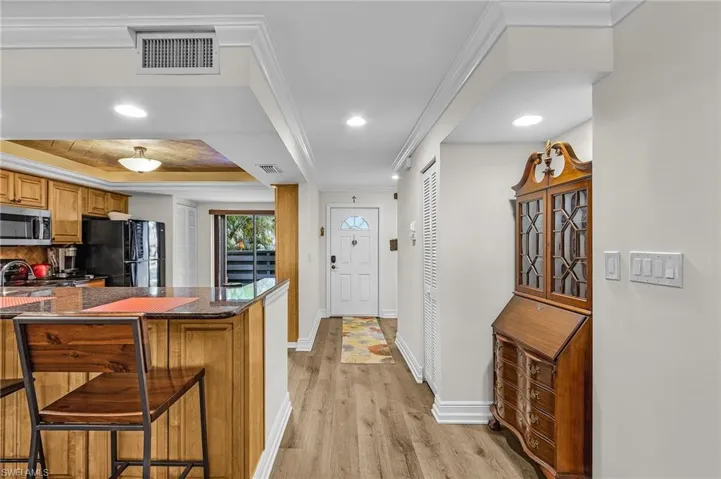 Kitchen with light wood finished floors, stainless steel microwave, visible vents, freestanding refrigerator, and a breakfast bar area