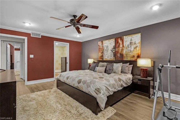 Bedroom with light wood-type flooring, baseboards, visible vents, and ornamental molding