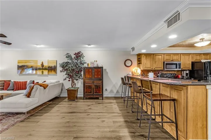 Kitchen featuring a kitchen breakfast bar, visible vents, stainless steel microwave, light wood-type flooring, and crown molding