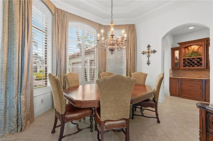 Dining space with a notable chandelier, a wealth of natural light, a raised ceiling, and crown molding