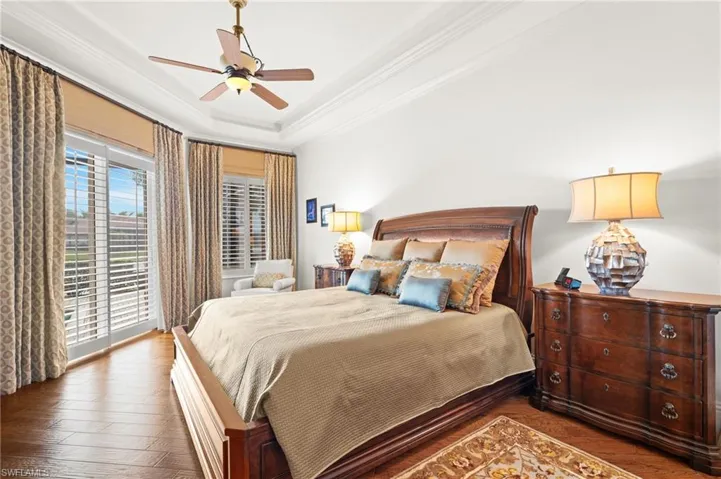 Bedroom with crown molding, ceiling fan, a raised ceiling, dark hardwood / wood-style flooring, and access to exterior