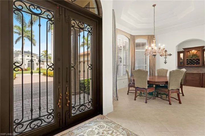 Tiled entrance foyer featuring french doors, ornamental molding, an inviting chandelier, and a tray ceiling