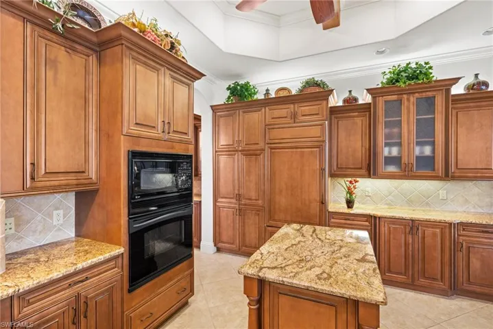 Kitchen with ceiling fan, backsplash, light stone counters, ornamental molding, and black appliances