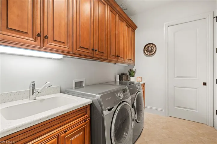 Clothes washing area featuring sink, light tile patterned flooring, cabinets, and washer and dryer